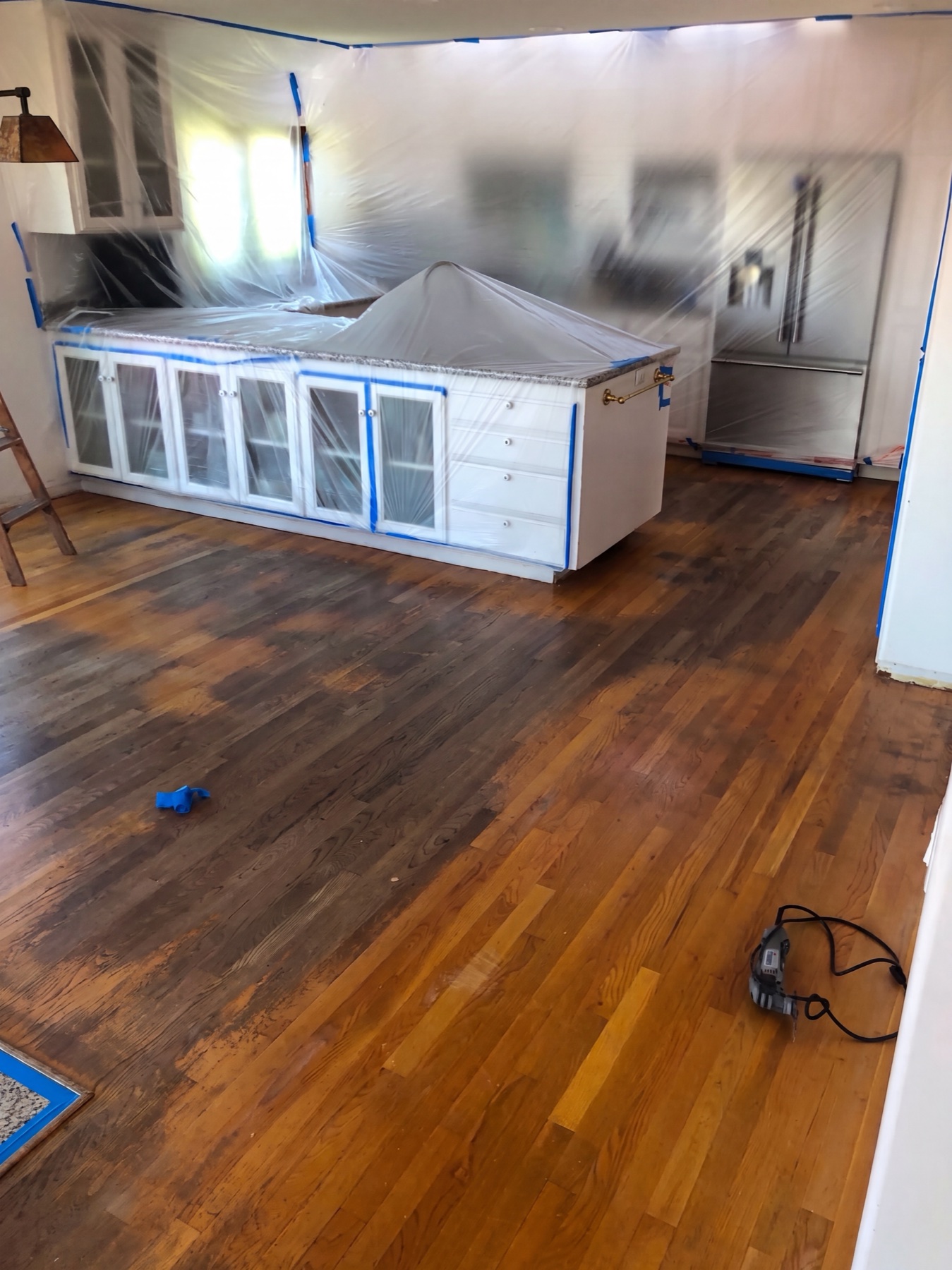 Kitchen floor mid-refinish — patchy, worn boards with the room masked off